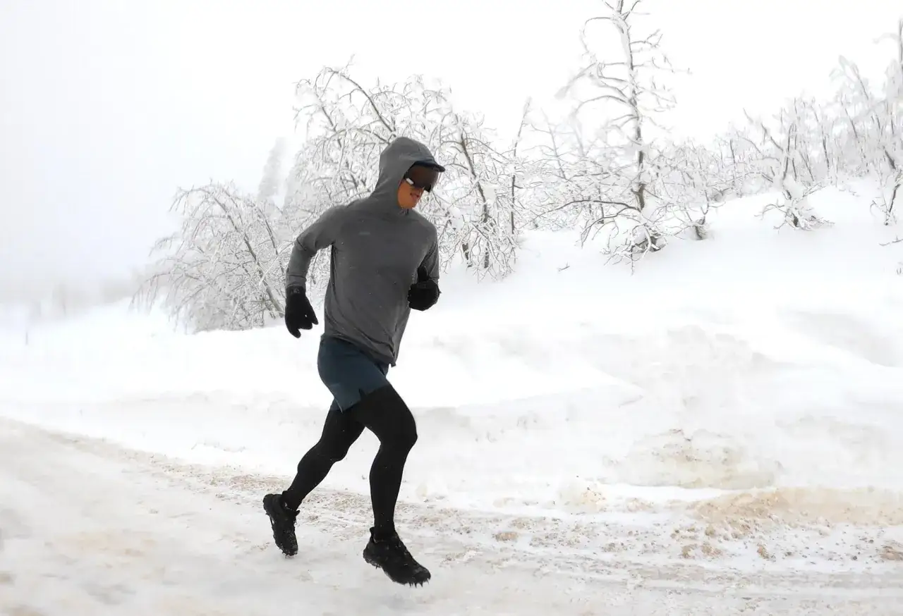 Un coureur d&eacute;termin&eacute; affronte le froid et la neige lors d'un running hivernal, entour&eacute; d'arbres givr&eacute;s.
