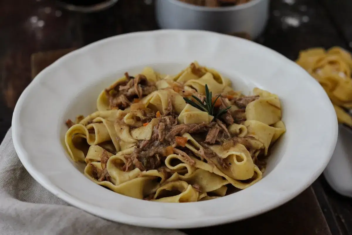 Pappardelle con ragù di carne, un classico dei primi piatti di carne, guarnite con rosmarino.