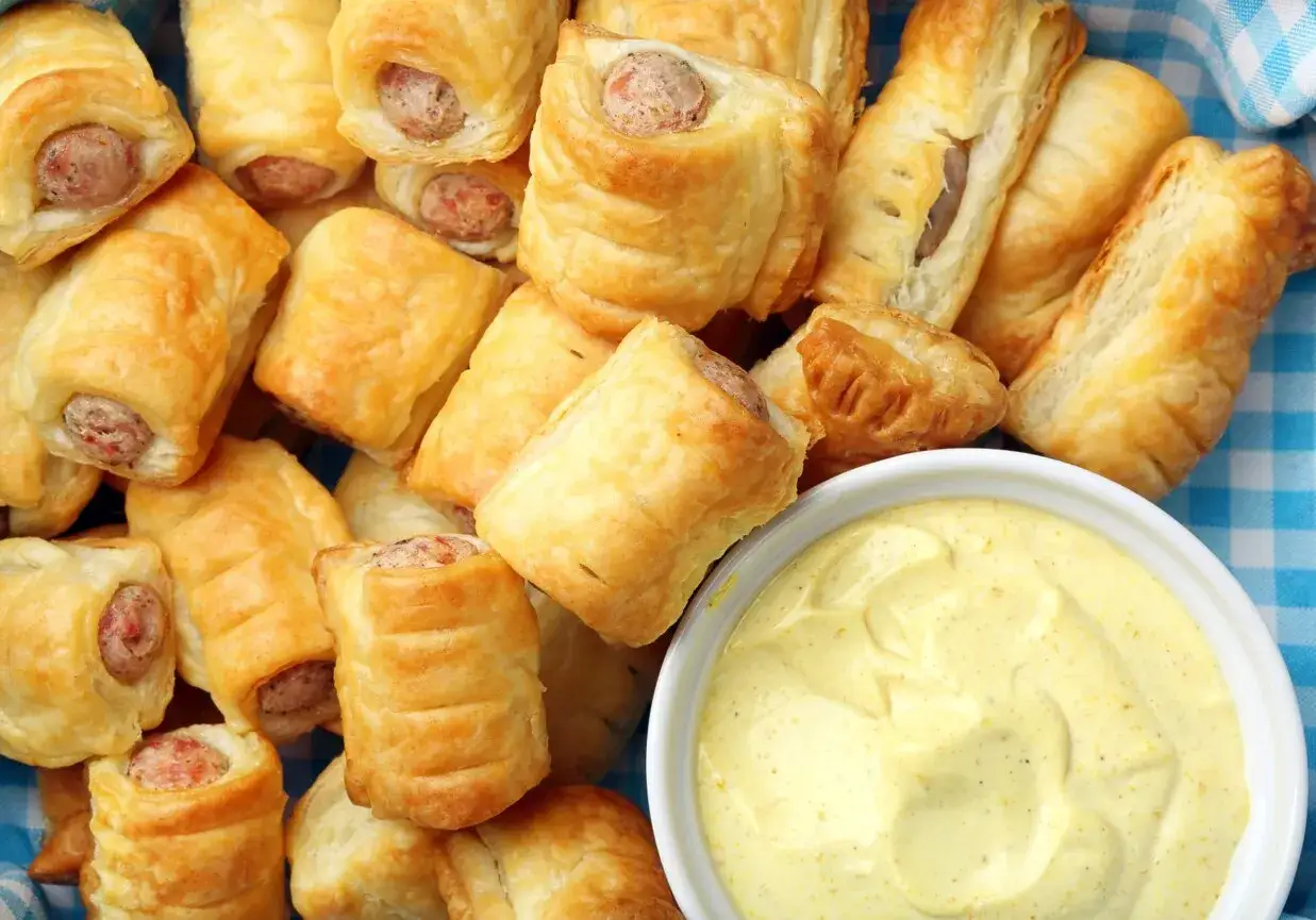 Złociste mini hot dogi w cieście francuskim, ułożone w koszyku, obok miseczki z musztardą. Idealne na imprezę!