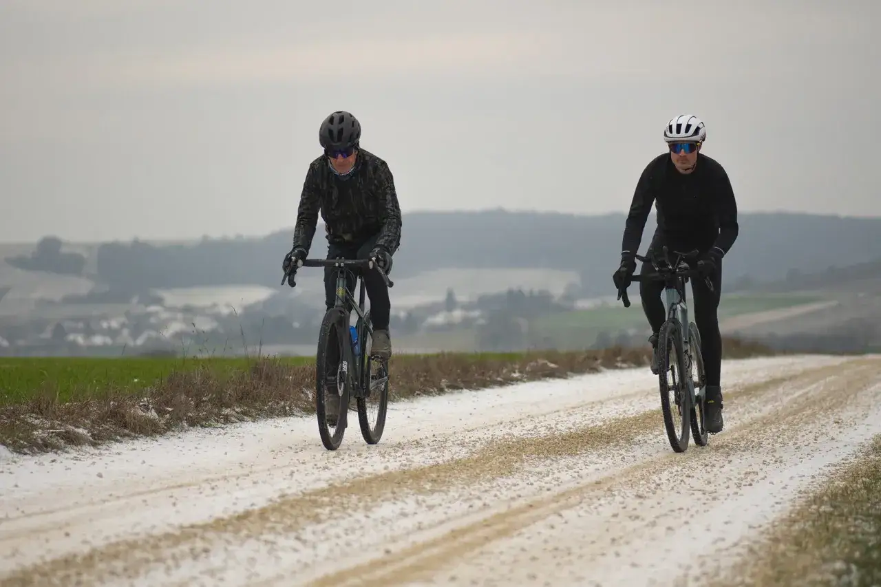 Deux cyclistes profitent d'une sortie gravel sur un chemin enneigé, paysage hivernal.