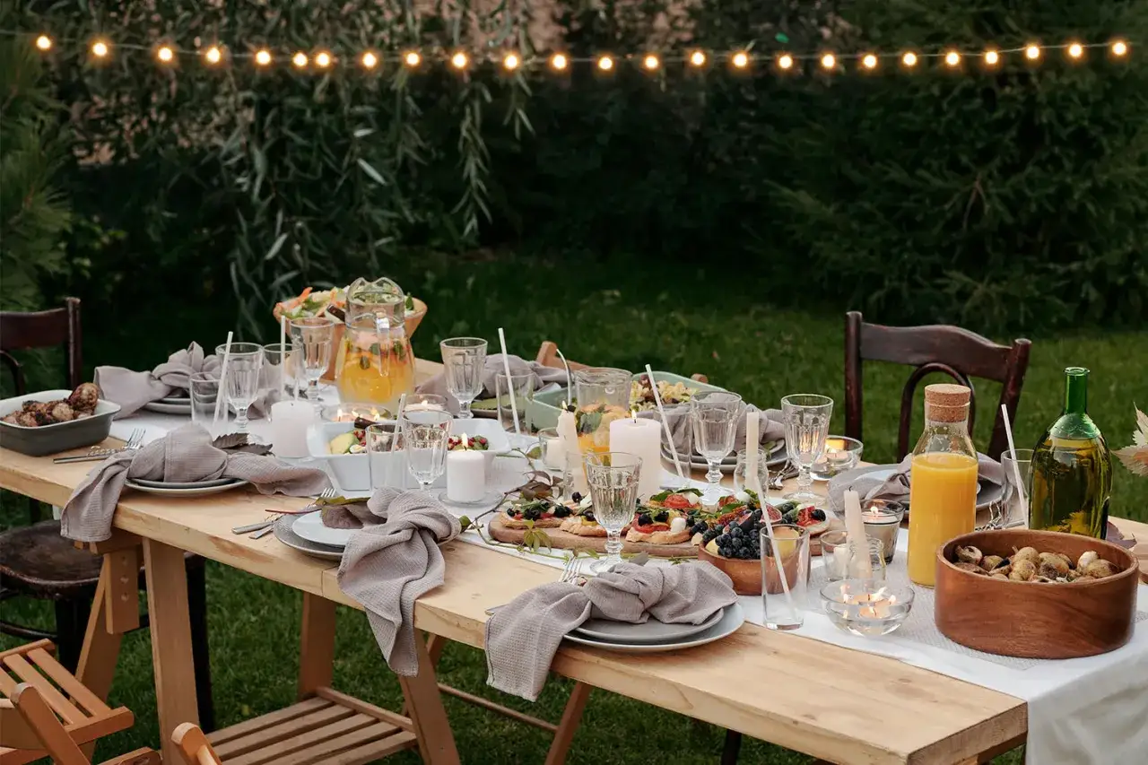 Une table dressée pour un brunch mariage en extérieur, avec des lumières guinguette, des plats variés, des boissons et des bougies.