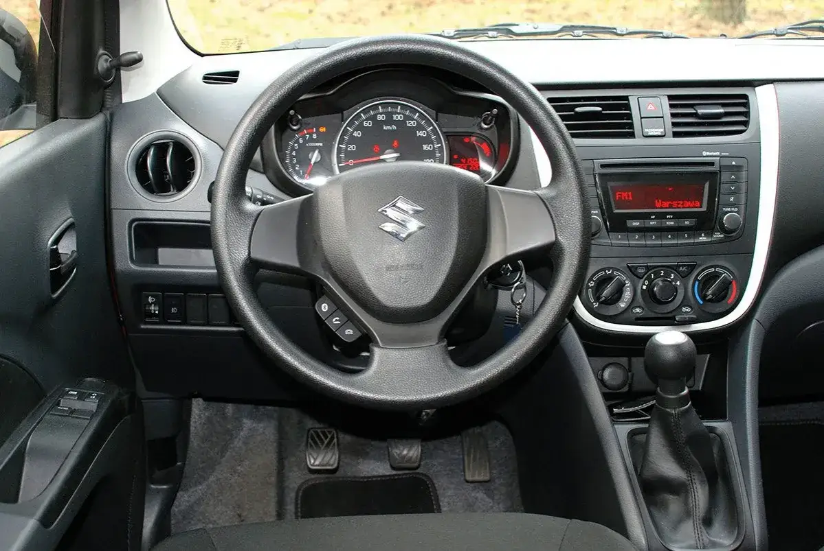 Wnętrze Suzuki Celerio: kierownica, deska rozdzielcza z radiem i nawiewami, dźwignia zmiany biegów.