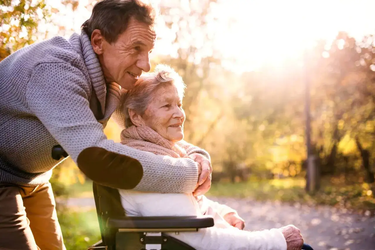 Un uomo abbraccia una donna in sedia a rotelle, un gesto d'amore che sottolinea l'importanza degli aiuti economici per malati di Alzheimer e per i loro cari.