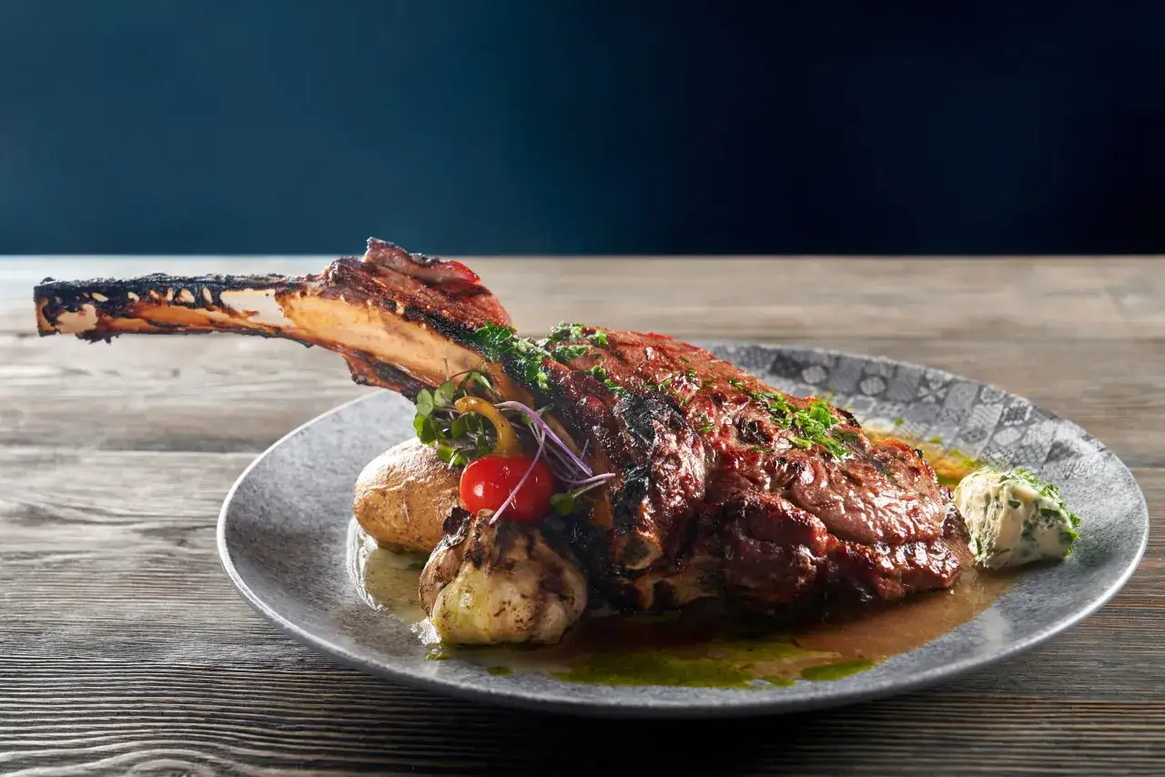 Un jugoso churrasco al horno con hueso, acompañado de patata asada, ajo y mantequilla de hierbas.