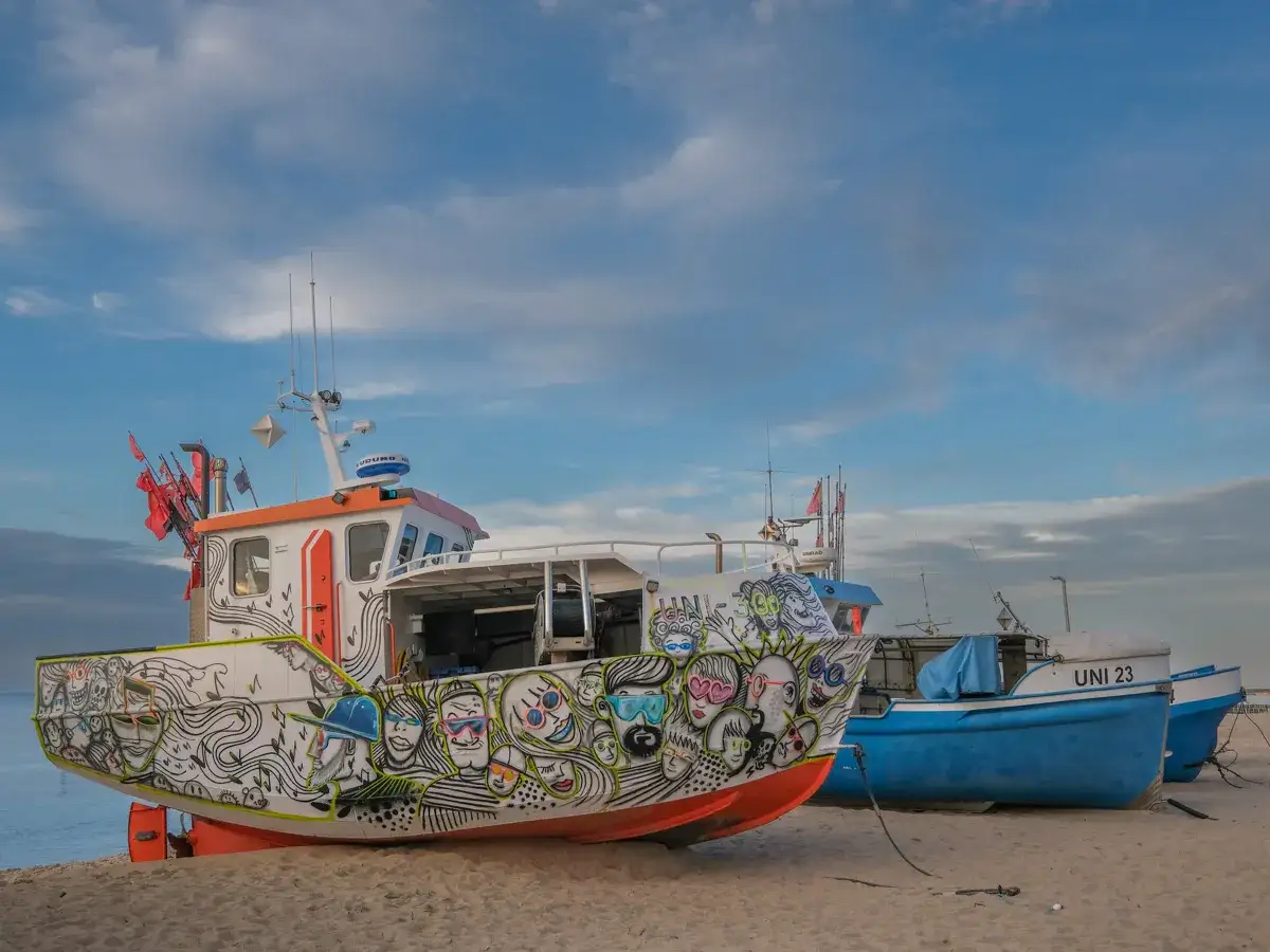 Kolorowe łodzie na plaży w Mielnie, z jedną ozdobioną zabawnymi rysunkami. To jedne z wielu atrakcji Mielna.
