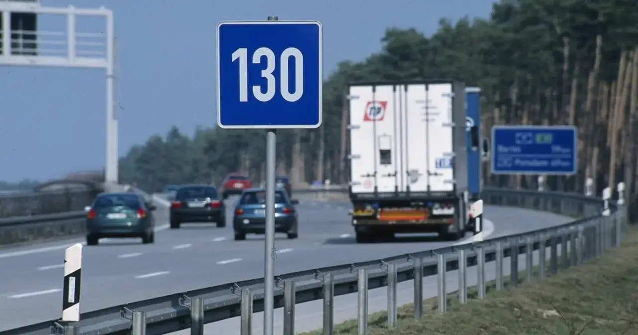 Znak ograniczenia prędkości 130 km/h na niemieckiej autostradzie. W tle ciężarówka i samochody osobowe.