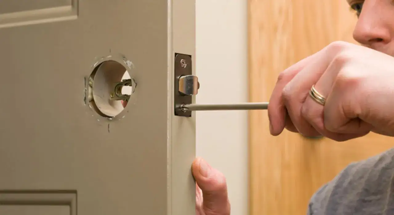 Un homme utilise un tournevis pour démonter une serrure, une étape pour savoir comment ouvrir une porte de chambre bloquée.