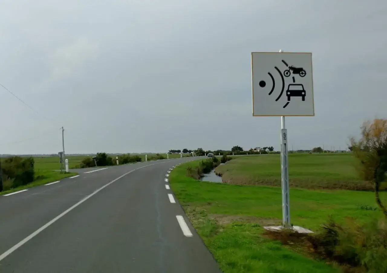 Znak informuje o systemie telepass we Francji. Droga prowadzi przez zielone tereny.