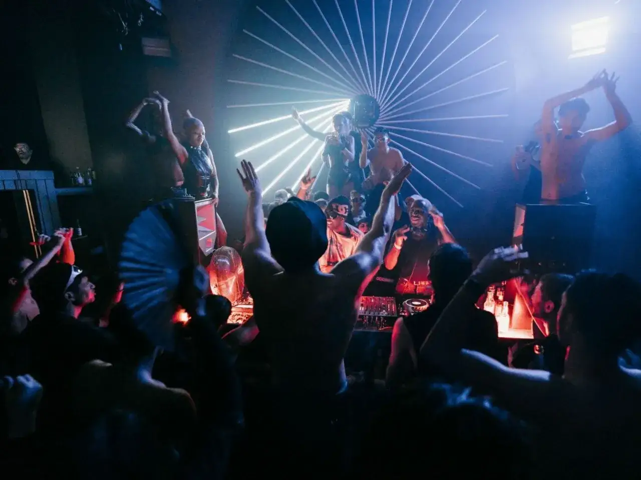 Un **berlino rave** vibrante con DJ, ballerini e folla in estasi sotto luci stroboscopiche e un'installazione luminosa a raggiera.
