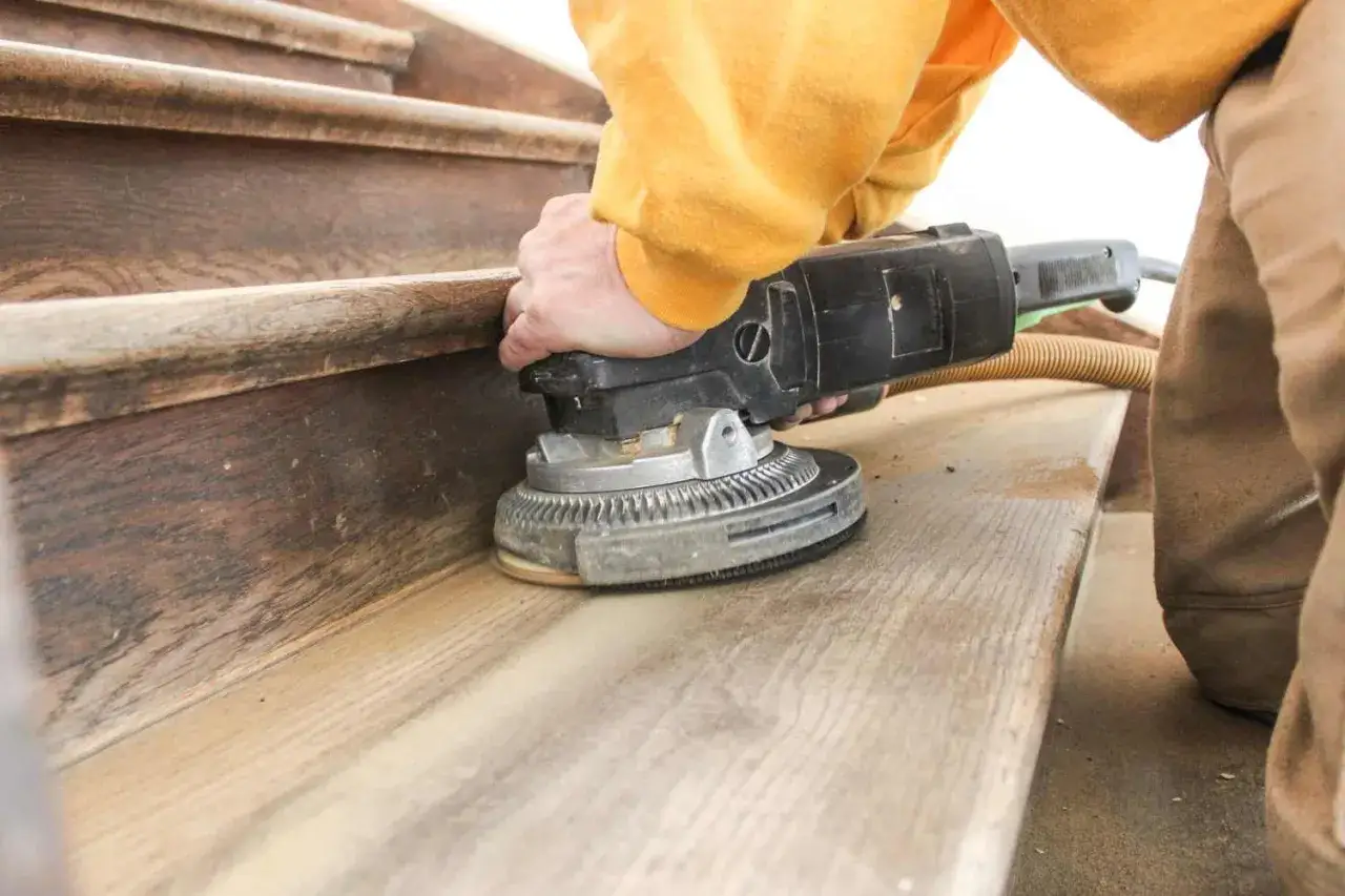 Hand schleift mit einer Maschine die Holztreppe, um den Boden f&uuml;r eine neue Behandlung vorzubereiten.