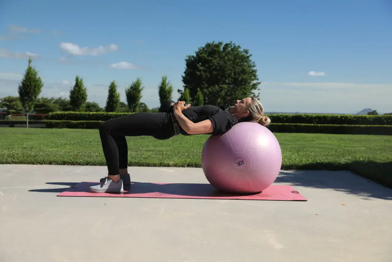 Mujer haciendo puente con pesa rusa sobre pelota de ejercicio, un ejercicio ideal para como activar las mitocondrias y mejorar la energía.