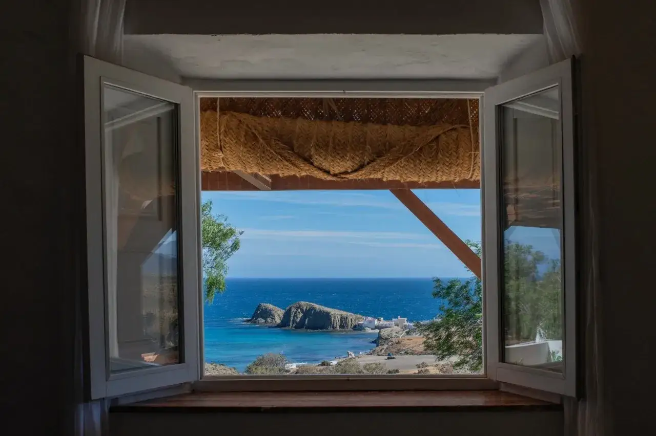 Ventana abierta en el cortijo La Loma, Almería, con vistas al mar azul y rocas.