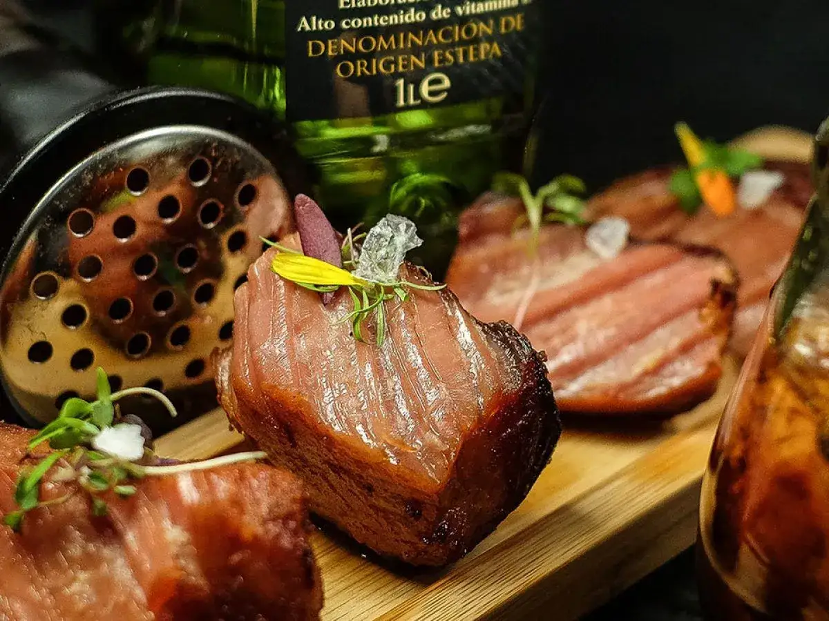 Delicioso lomo de orza, tierno y jugoso, servido en tabla de madera con guarnici&oacute;n de brotes verdes.