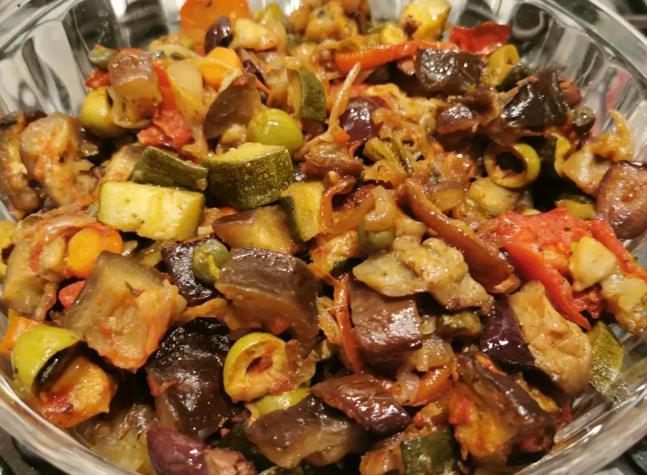 Un plat coloré de recette caponata sicilienne traditionnelle au four, avec aubergines, courgettes, olives et tomates.