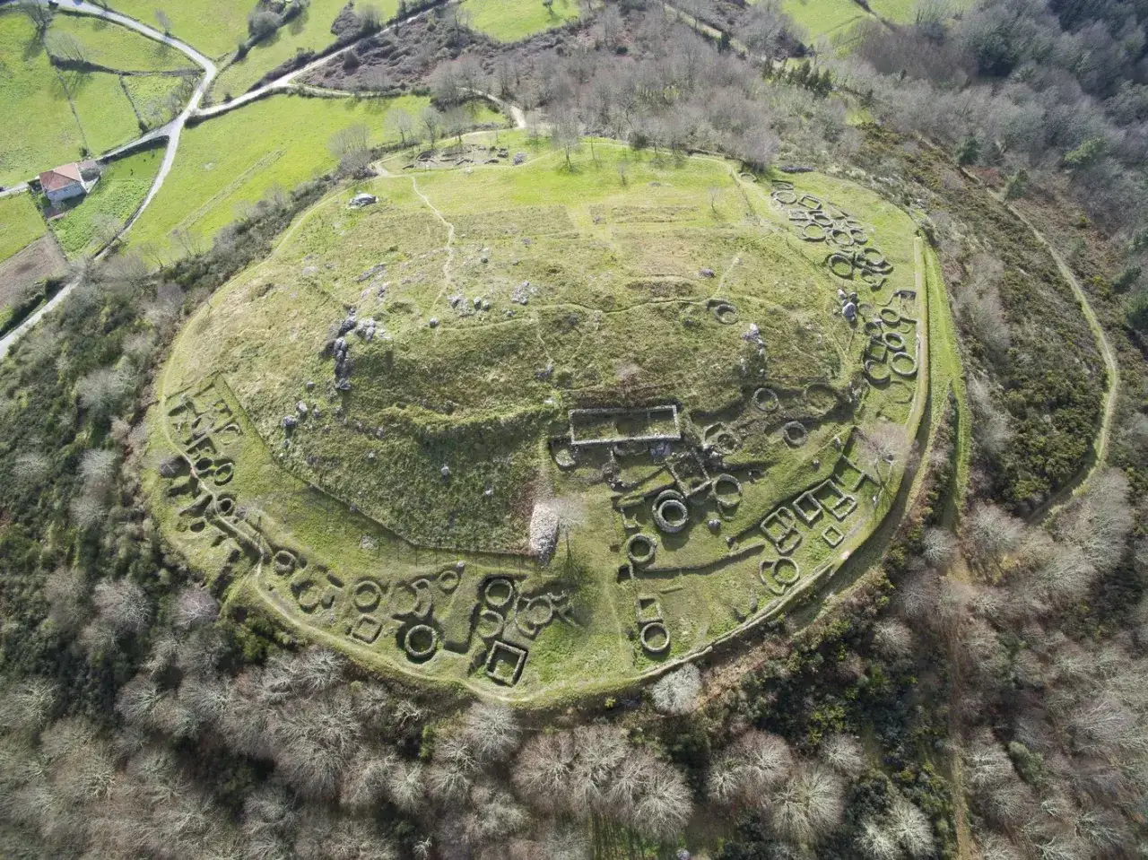 Vista aérea del castro de San Cibrao de Las, un yacimiento arqueológico en Celanova, Galicia, con restos de construcciones circulares y rectangulares.