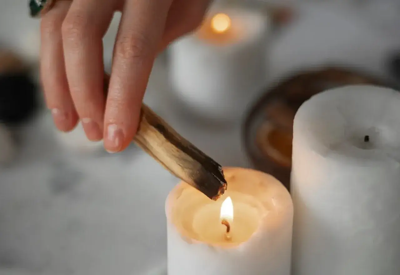 Mano enciende un palo santo sobre una vela, iniciando un ritual de purificaci&oacute;n.