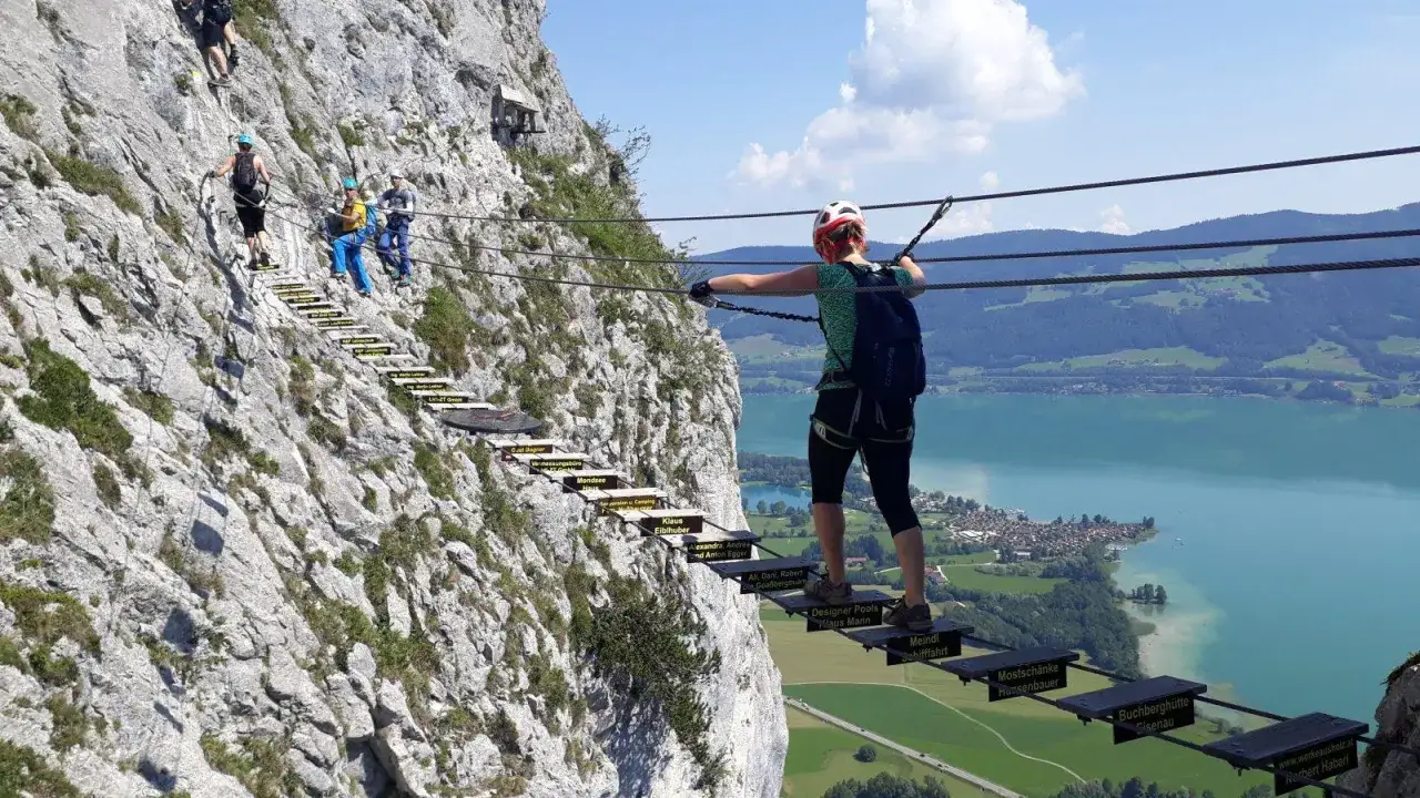Via ferrata w Niemczech: grupa ludzi pokonuje skalną ścieżkę z drabinkami i linami, podziwiając malowniczy widok na jezioro.