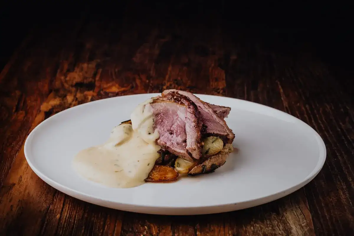 Tranches de rumsteak d'agneau rosées, nappées d'une sauce crémeuse, servies sur des pommes de terre rôties.
