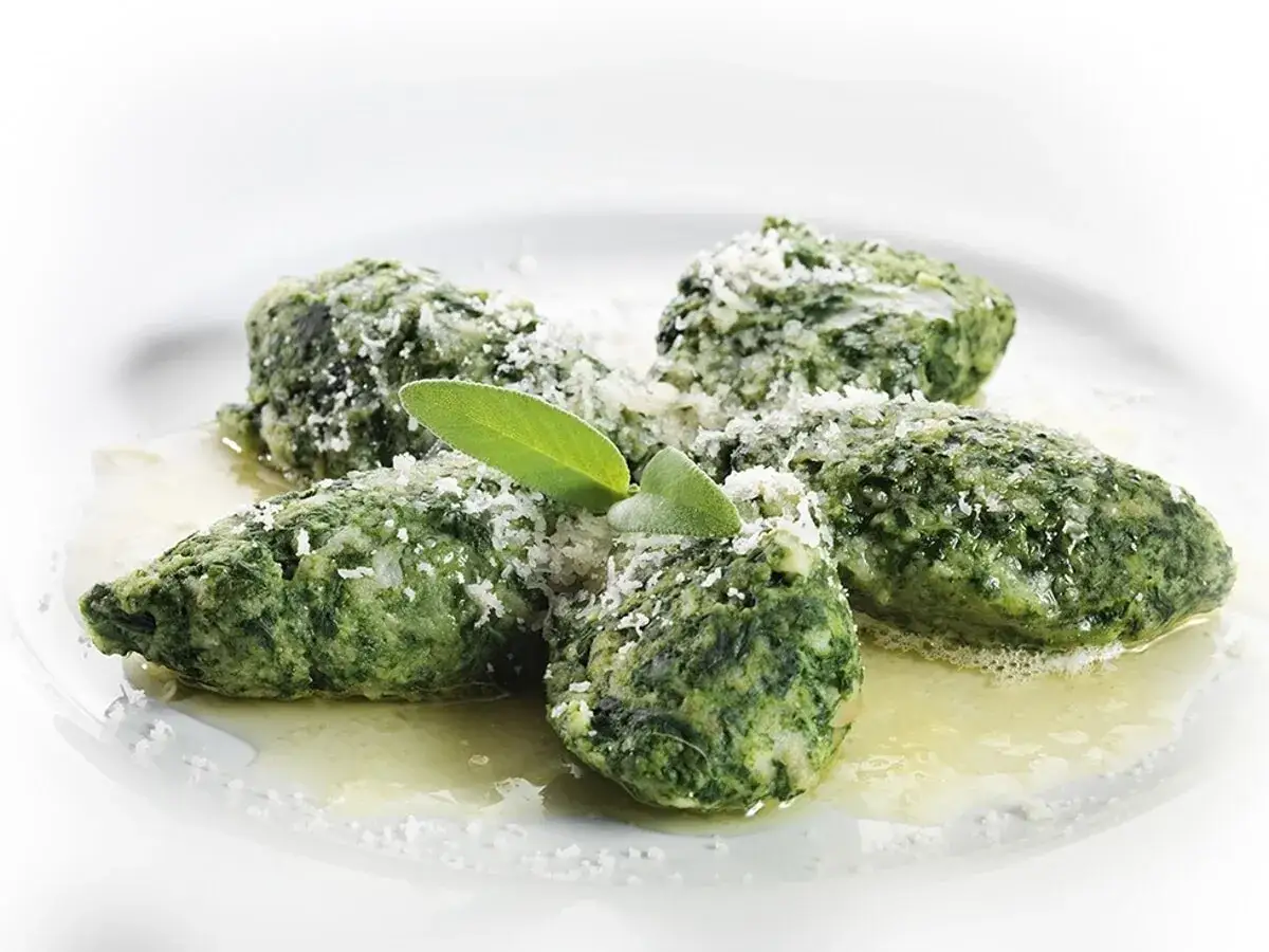 Strangolapreti alla trentina, gustosi gnocchi verdi con burro fuso, parmigiano e una foglia di salvia.