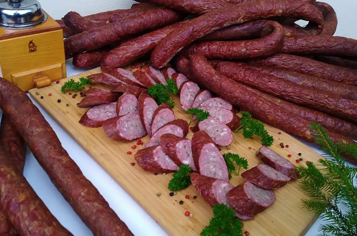 Kiełbasa z dzika, pokrojona w plastry, ułożona na desce z ziołami i pieprzem. Idealna na przepis na kiełbasę z dzika.