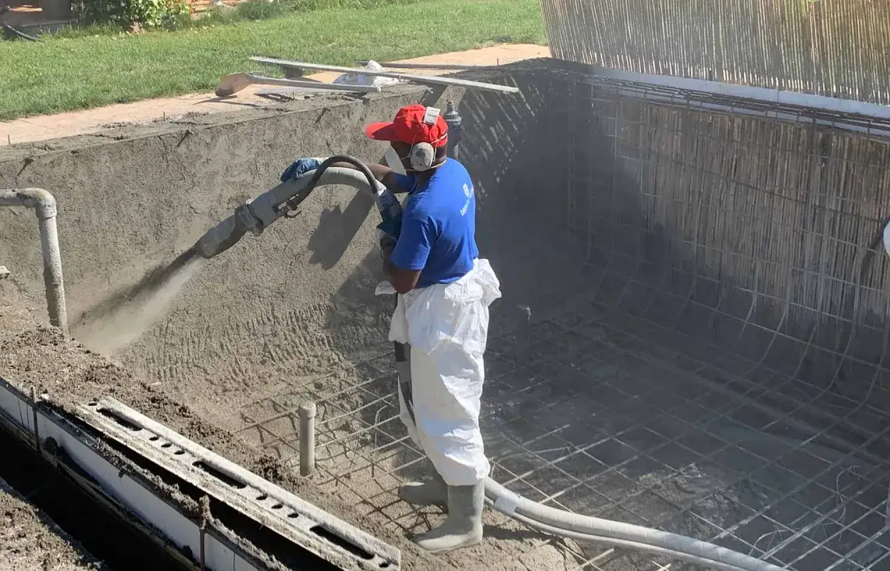 Un ouvrier projette du béton pour créer un bassin en béton étanche. La structure métallique est visible.