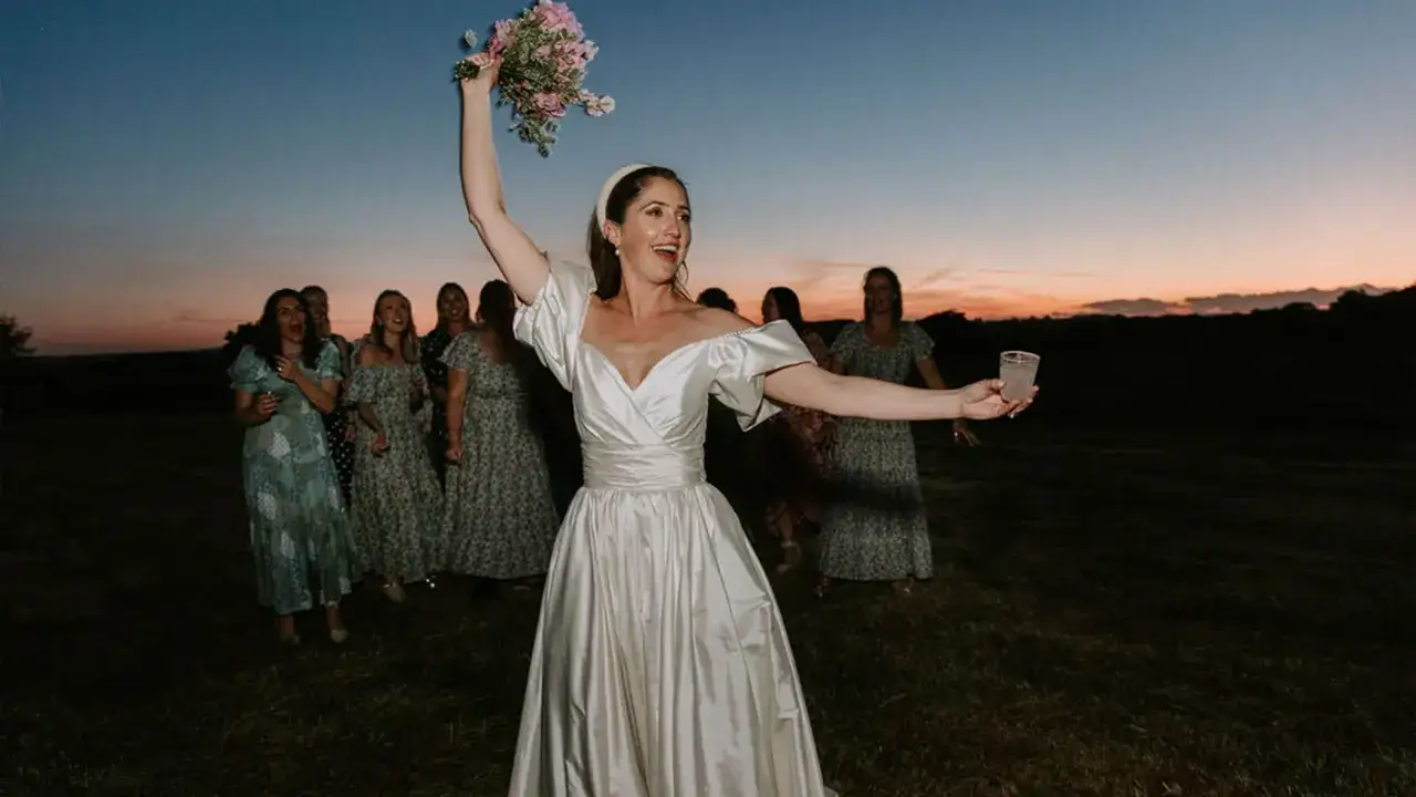 Braut wirft Blumenstrau&szlig; bei einer englischen Hochzeit im Abendlicht. Brautjungfern warten gespannt.