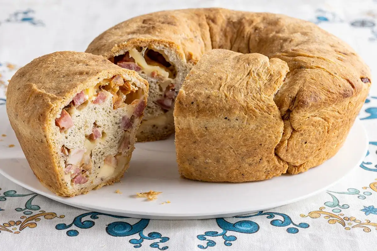 Casatiello napoletano ricetta della nonna: un impasto dorato ripieno di salumi e formaggio, tagliato per mostrarne la bontà.