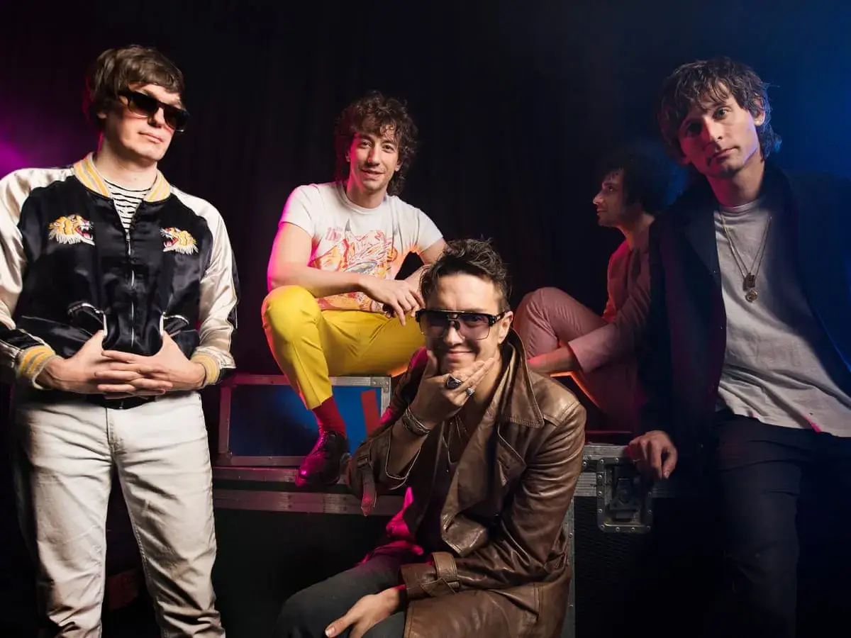 Les membres de The Strokes posent ensemble, éclairés par des lumières bleues et roses.