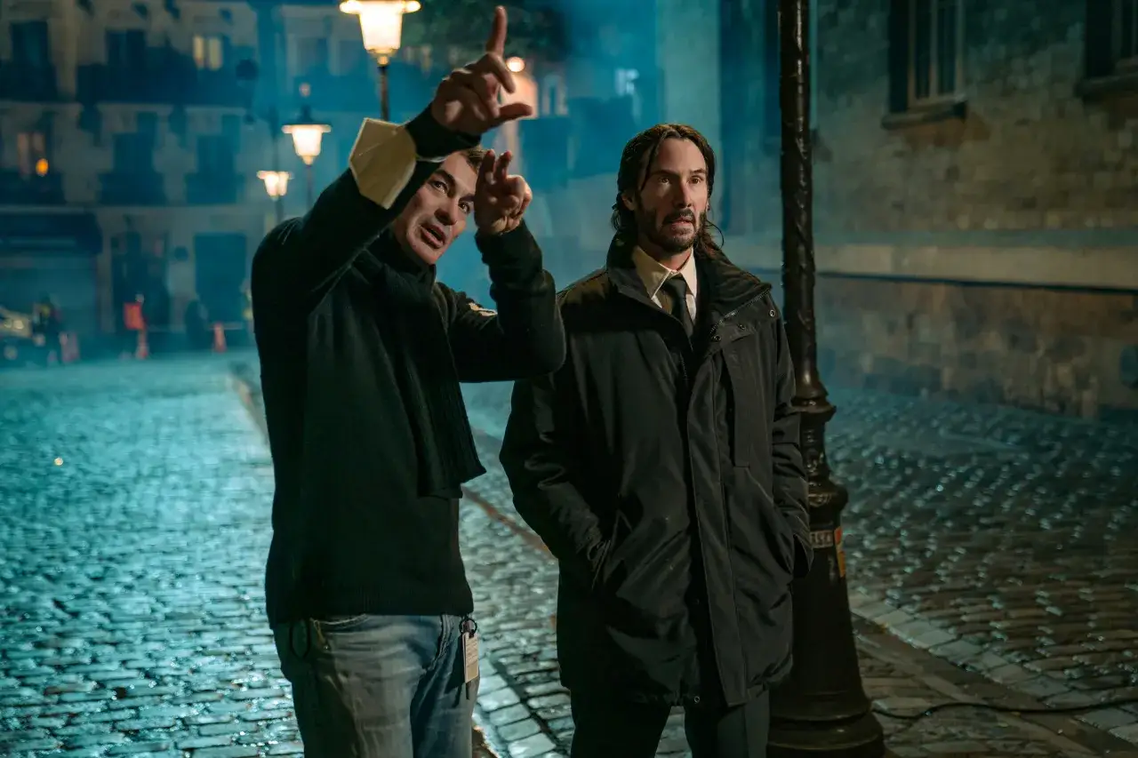 Reżyser instruuje Keanu Reevesa, który wciela się w Johna Wicka. Czy John Wick umiera? Scena nocna na brukowanej ulicy.