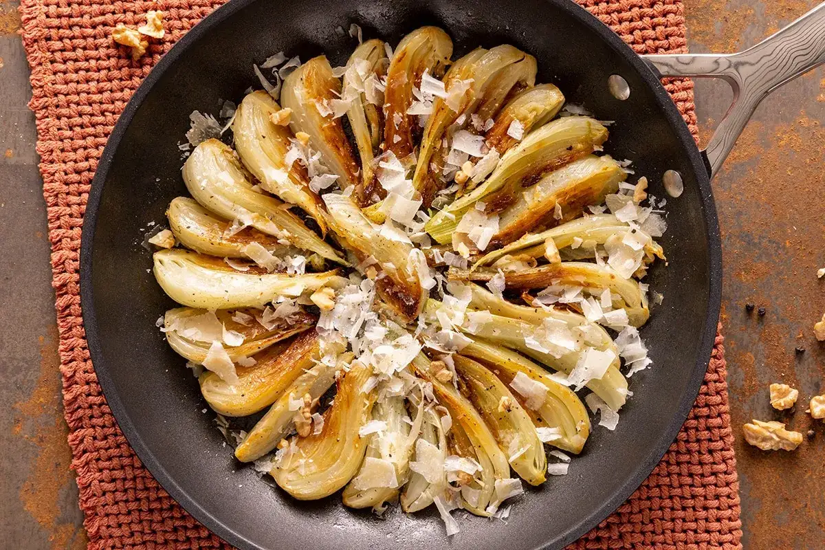 Finocchi in padella dorati e saporiti, guarniti con scaglie di formaggio e noci croccanti. Un contorno delizioso e facile da preparare.