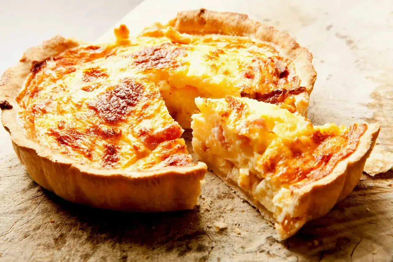 Une quiche lorraine, une des spécialités de Metz, avec une part coupée, révélant sa garniture crémeuse et ses lardons.