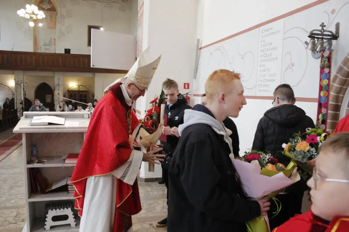 Biskup, kto to jest szafarz bierzmowania, wręcza bukiet młodemu mężczyźnie podczas uroczystości w kościele.