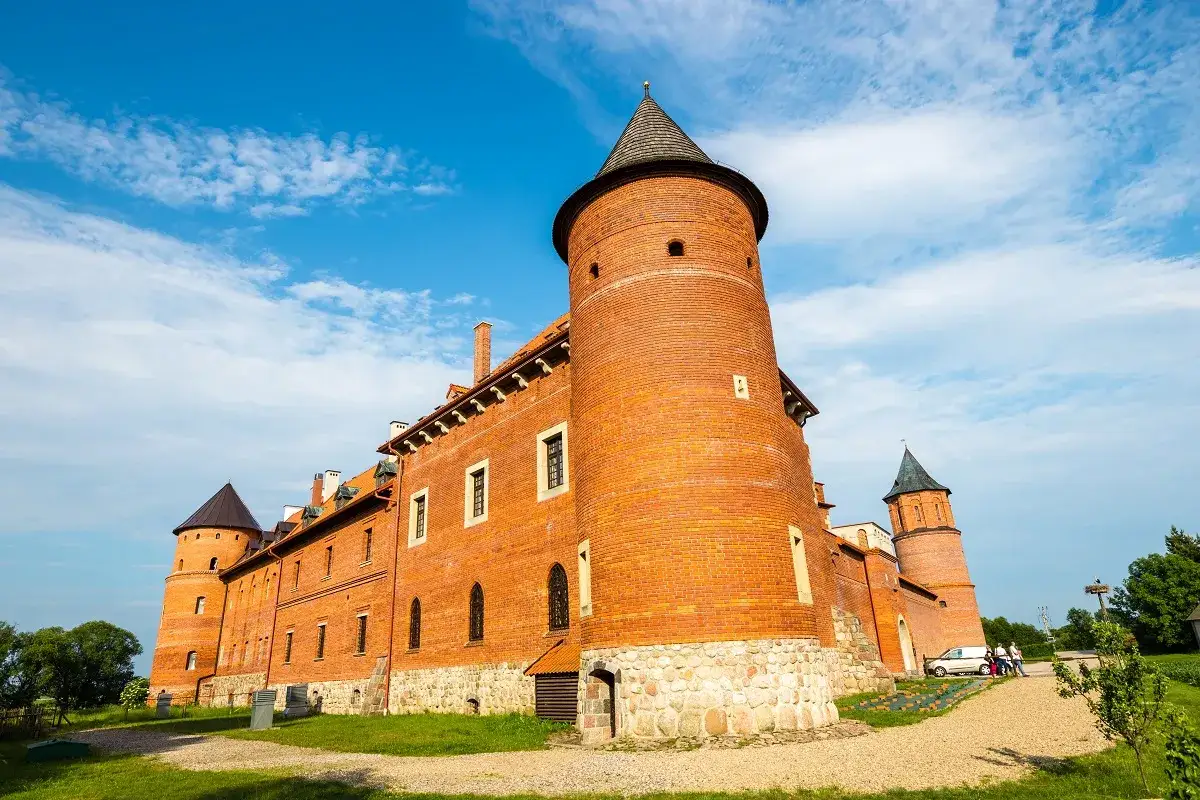 Zamek w Tykocinie, jedna z nietypowych atrakcji Podlasia, z ceglanymi wieżami i kamiennym cokołem, pod błękitnym niebem.