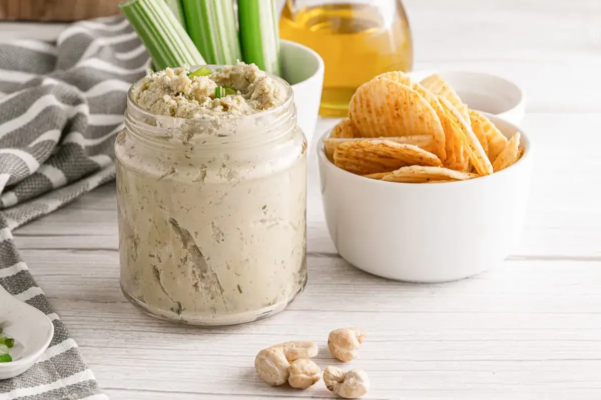 Tarro de cremoso queso vegano con apio, patatas fritas y anacardos.