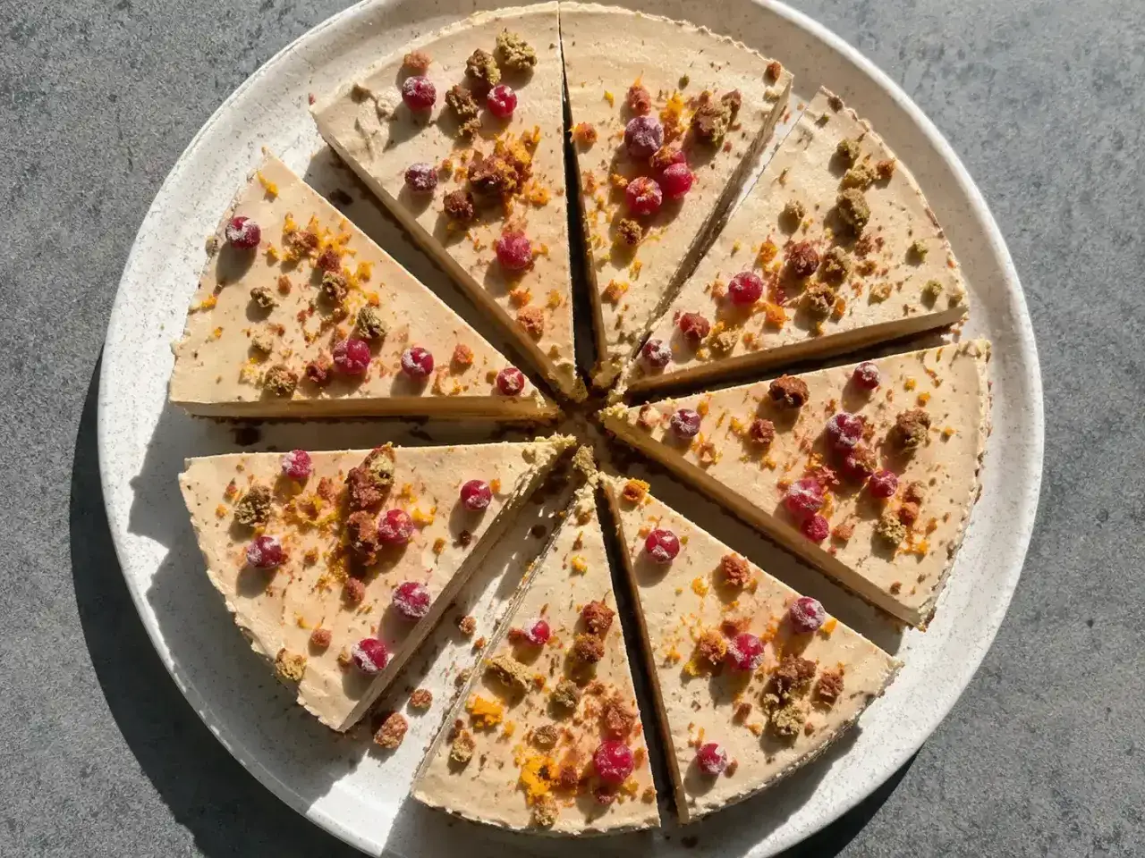 En skivad cheesecake med pepparkaksbotten, toppad med röda bär och smulor.