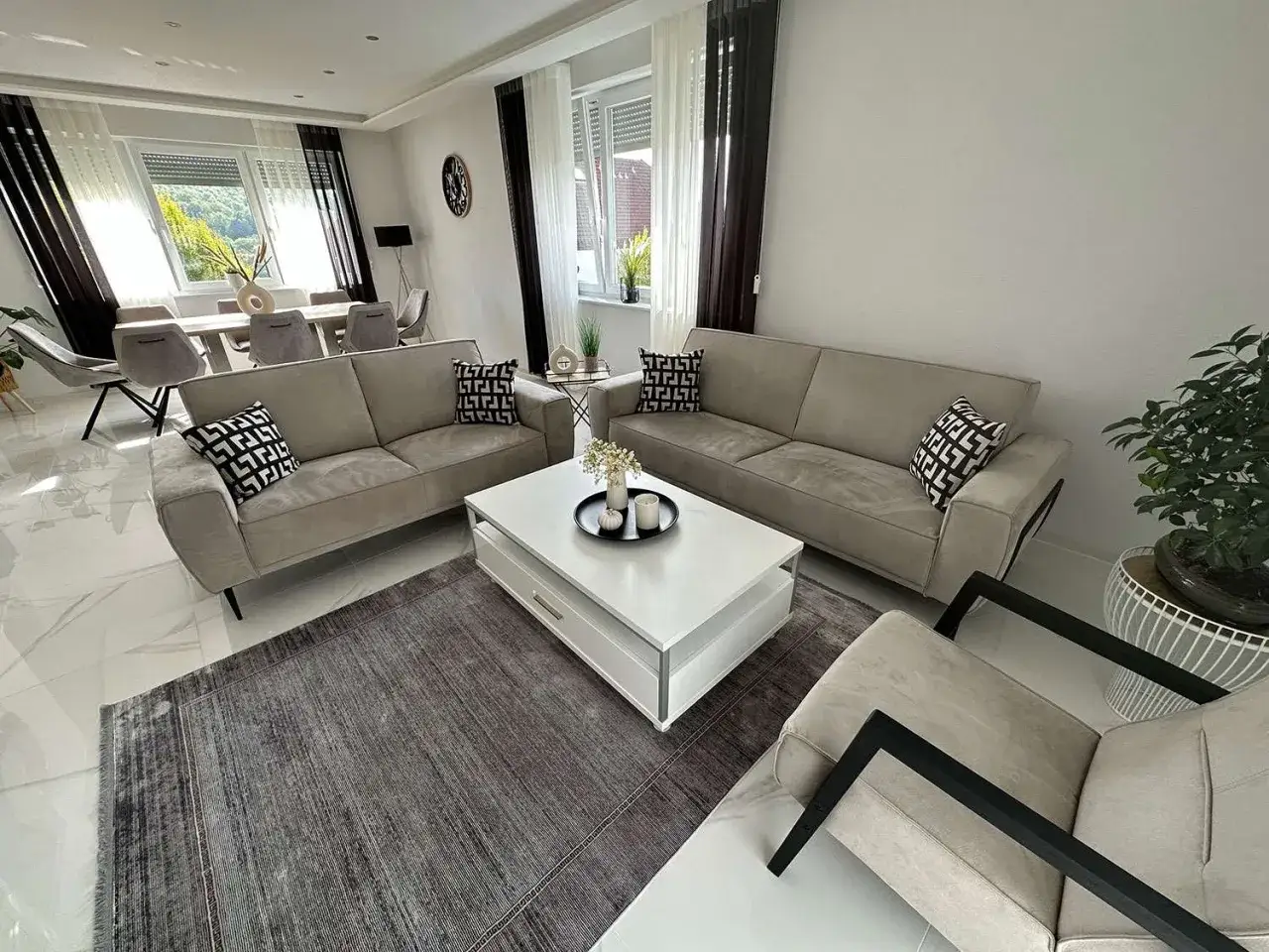 Elegantes Wohnzimmer: Sofas und Sessel in hellen Beige-Tönen, kombiniert mit einem grauen Teppich und schwarzen Akzenten.