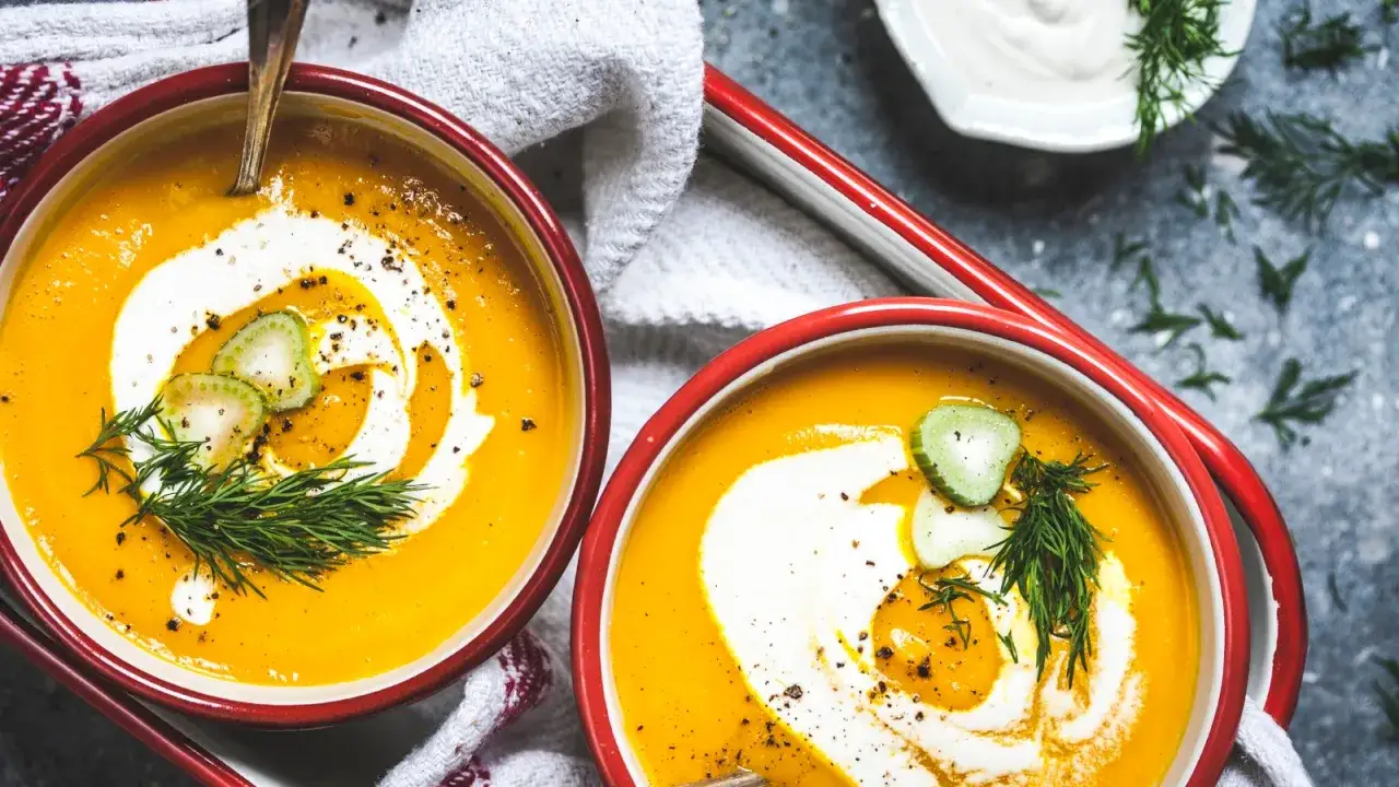Zwei Schüsseln cremiger Kürbissuppe, verziert mit einem Swirl aus Schlagsahne, Gurkenscheiben und Dill. Ja, man kann Schlagsahne zum Kochen nehmen, um Suppen zu verfeinern.