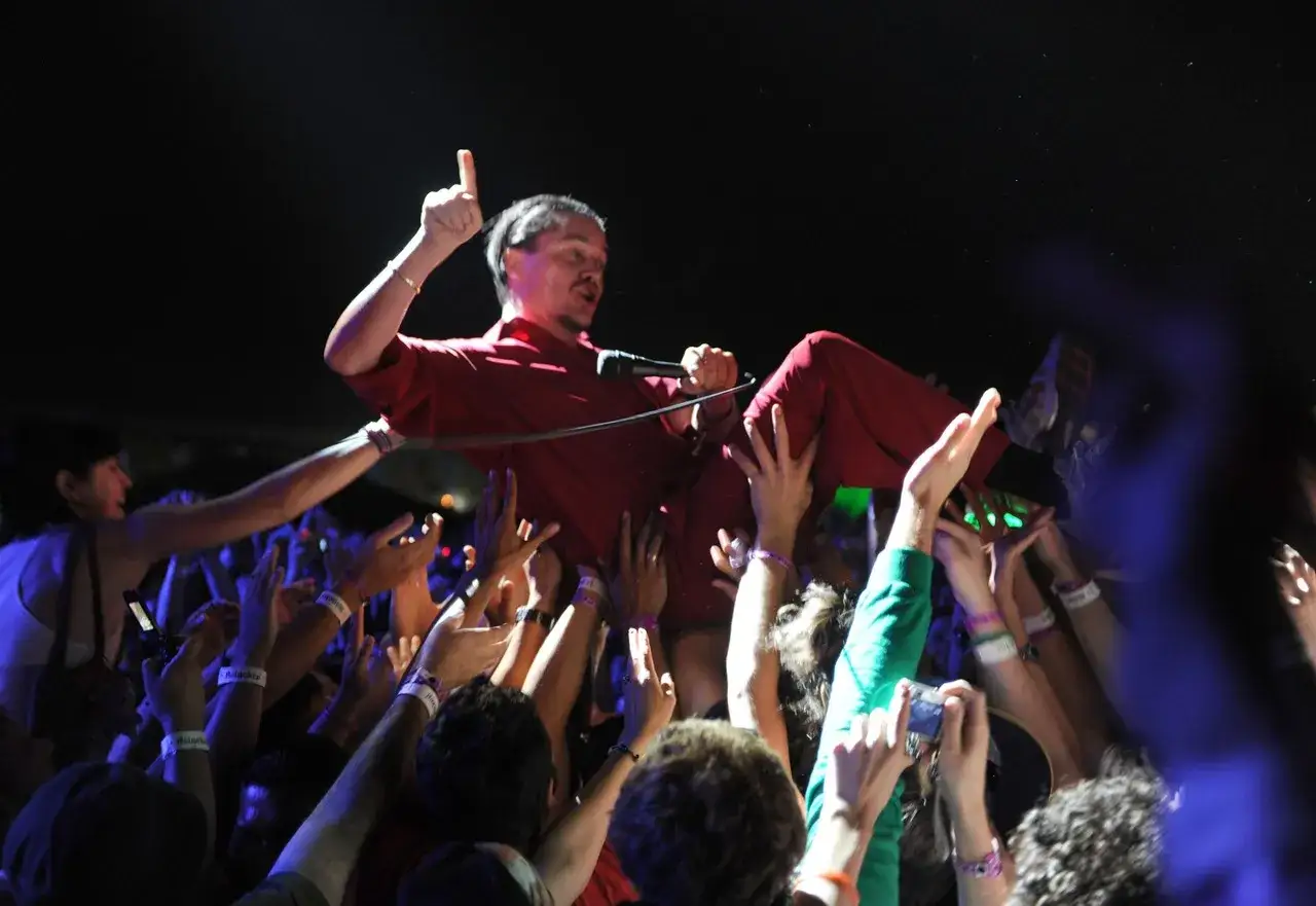 Mike Patton heute: Der S&auml;nger wird von der Menge getragen, Mikrofon in der Hand, ein Finger zeigt nach oben.