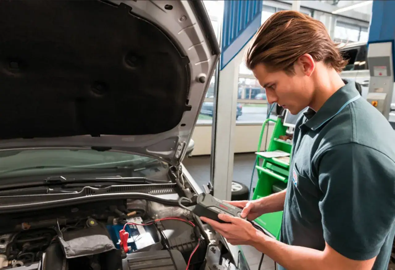 Mekaniker kontrollerar bilbatteriet med en diagnosenhet i en auktoriserad verkstad.