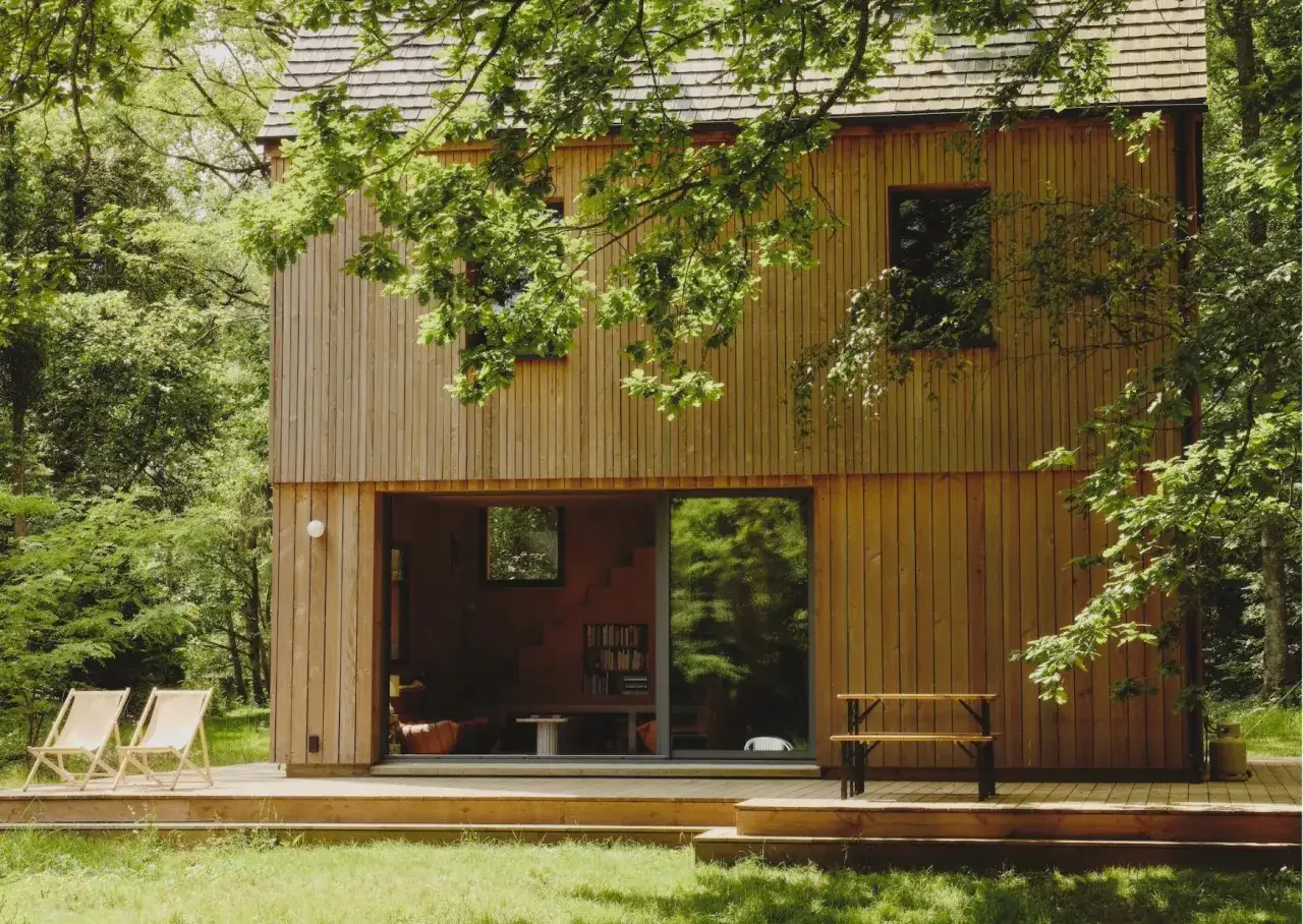 Tiny house en bois nichée dans une forêt verdoyante. Deux chaises longues sur la terrasse invitent à la détente.