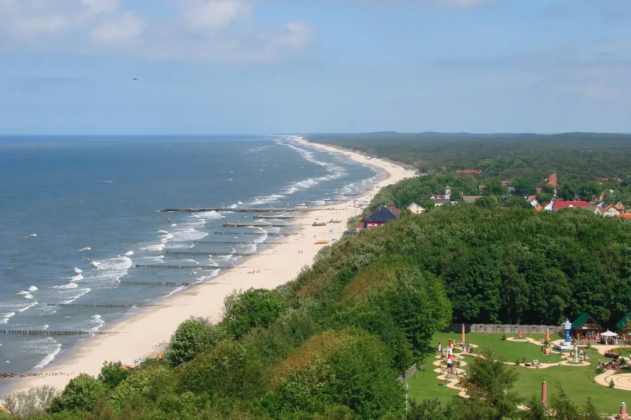 Widok z klifu w Rewalu na plażę, morze i las. W oddali widać zabudowania, a na pierwszym planie zielony teren z atrakcjami. Idealne miejsce na camping.
