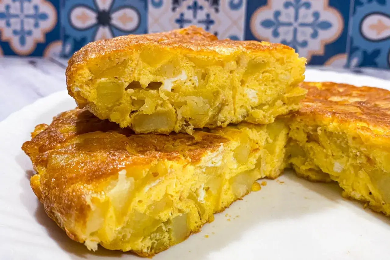 Fetta di frittata di patate dorata e soffice, con pezzi di patate ben visibili nell'uovo.