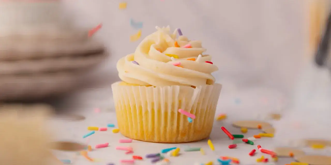 Un cupcake orné d'un glacage cupcake vanille crémeux, parsemé de vermicelles colorés tombant comme une pluie festive.