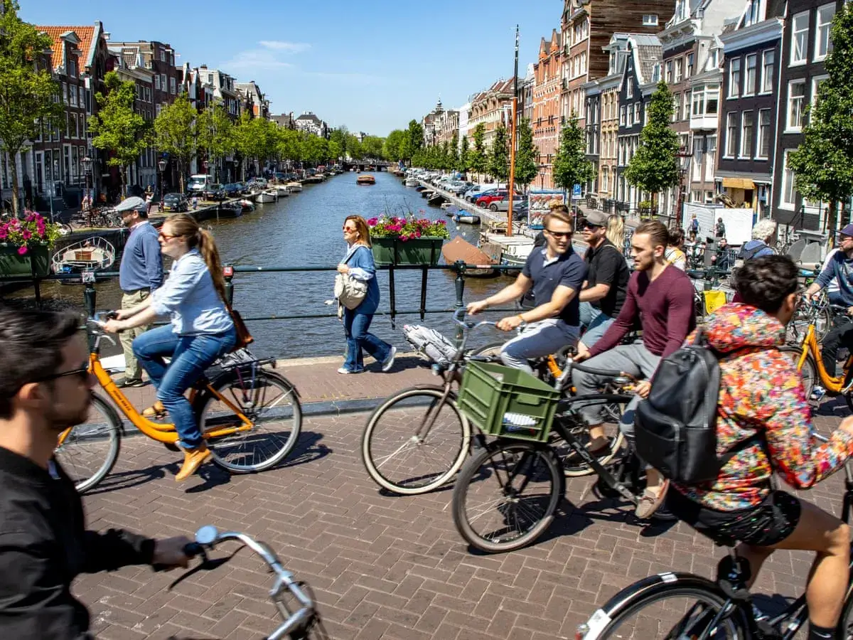 Gente en bicicleta por un canal de Ámsterdam, un consejo para viajar a Ámsterdam es disfrutar de su ambiente ciclista.