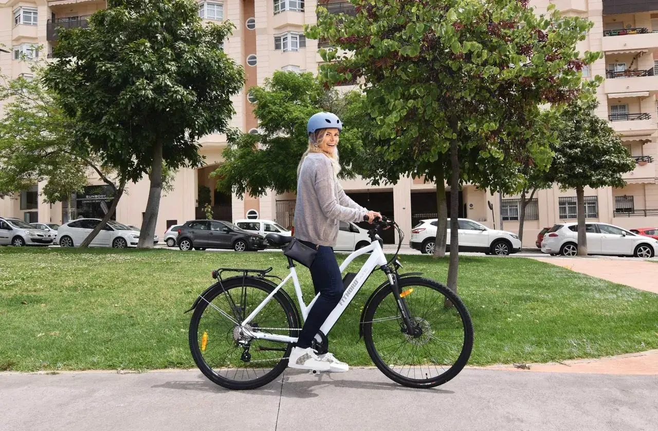 Glad kvinna på elcykel i stadsmiljö. Frågan