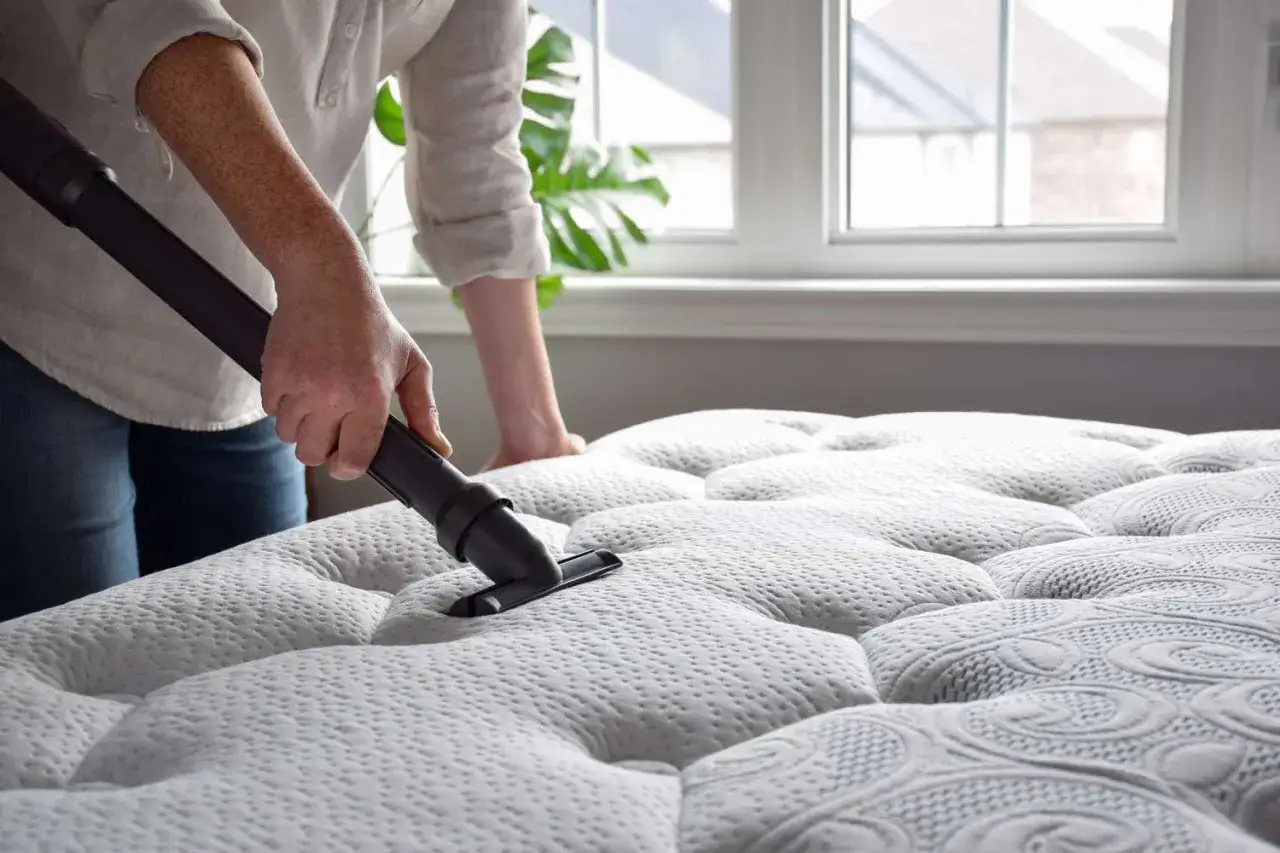 Vacuuming a mattress topper to remove dust and odors, hoping to eliminate the lingering sweat smell.