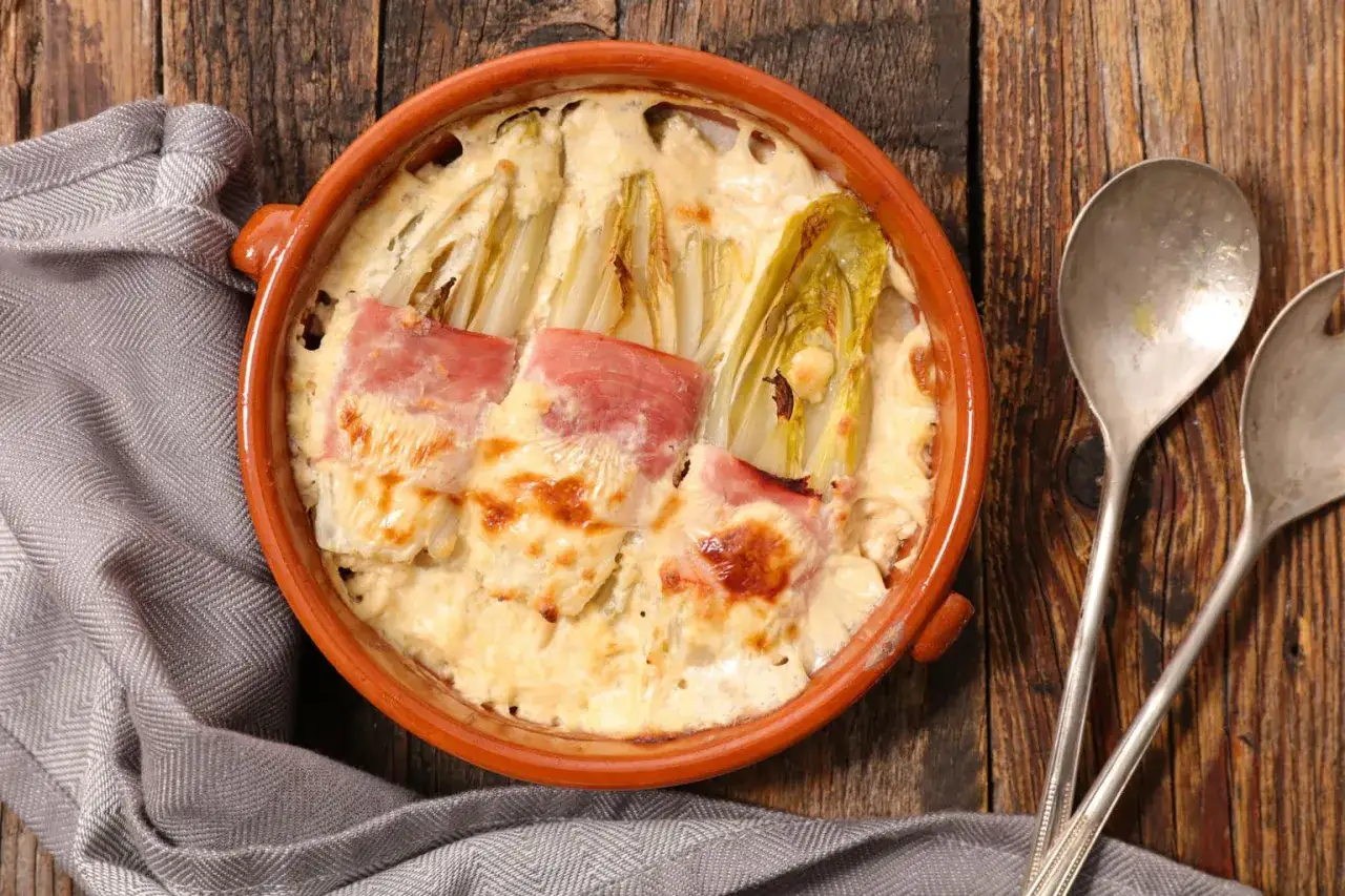 Endivias a la plancha con jamón, gratinadas en una cazuela de barro con una cremosa salsa.