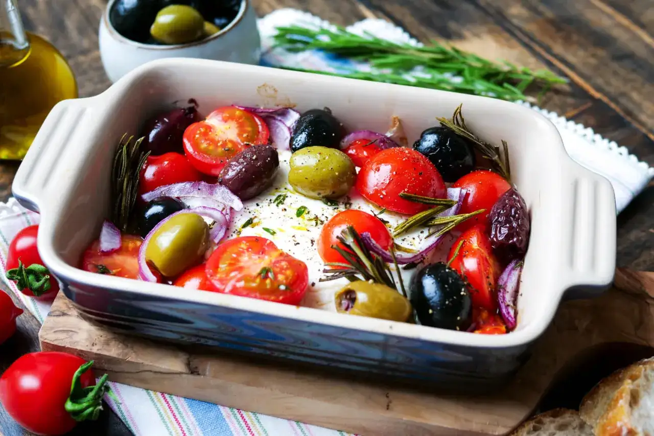 Gebackener Feta mit Kirschtomaten, Oliven und Rosmarin in einer Auflaufform.