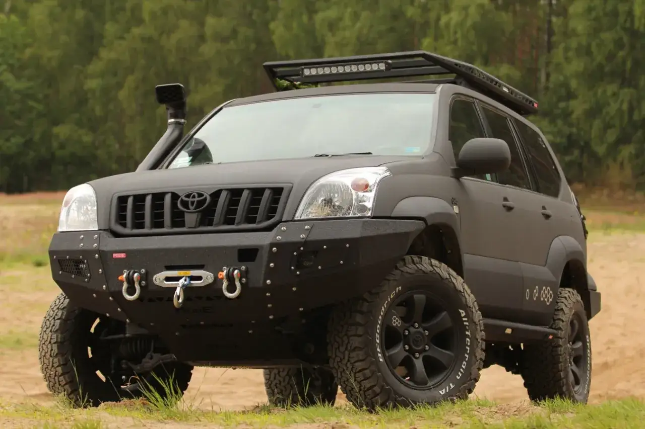 Czarny, zmodyfikowany Land Cruiser 120 z wyciągarką, snorkel'em i bagażnikiem dachowym, gotowy na terenową przygodę.