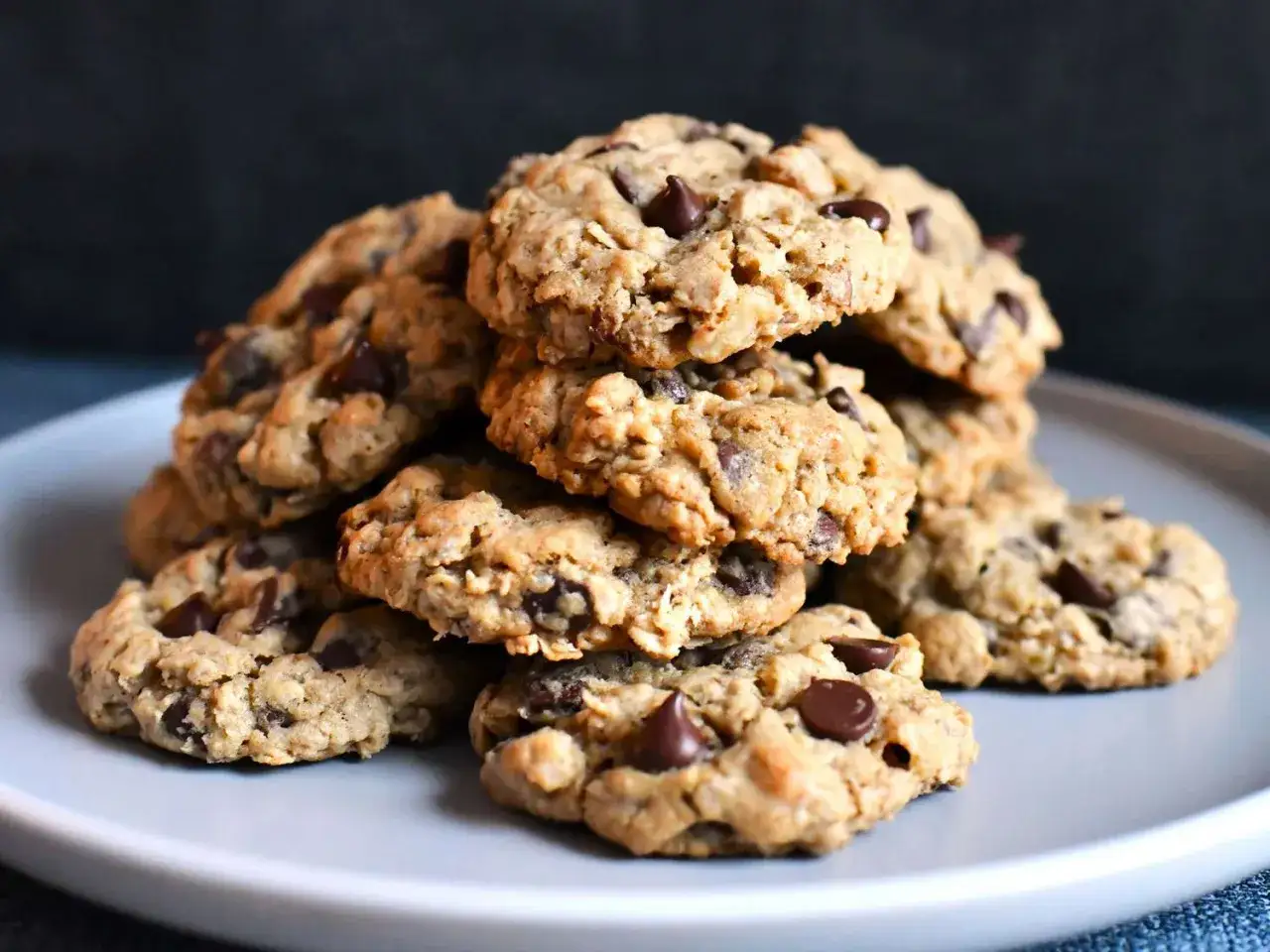 Montón de galletas de avena y chocolate caseras, con trozos de chocolate derretido, apiladas en un plato gris.